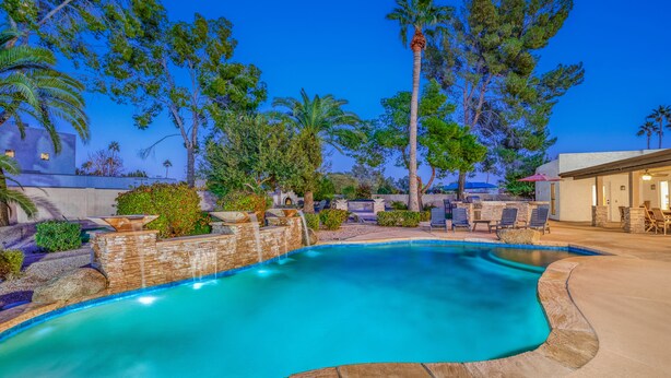 A swimming pool with a stone border, surrounded by palm trees and a patio area with outdoor furniture. - Centrally located estate in Scottsdale with a heated pool, game room, and more! (Scottsdale)