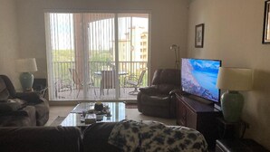 Una sala de estar con sofá, televisor, mesa de centro y balcón con vista a edificios.