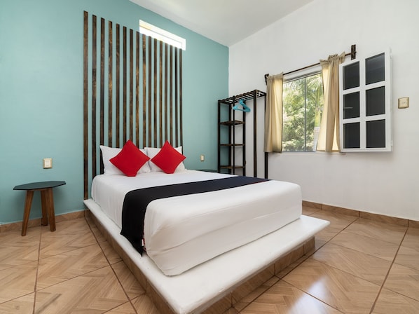 Un dormitorio ordenado con una cama, una mesita y una ventana con cortinas.