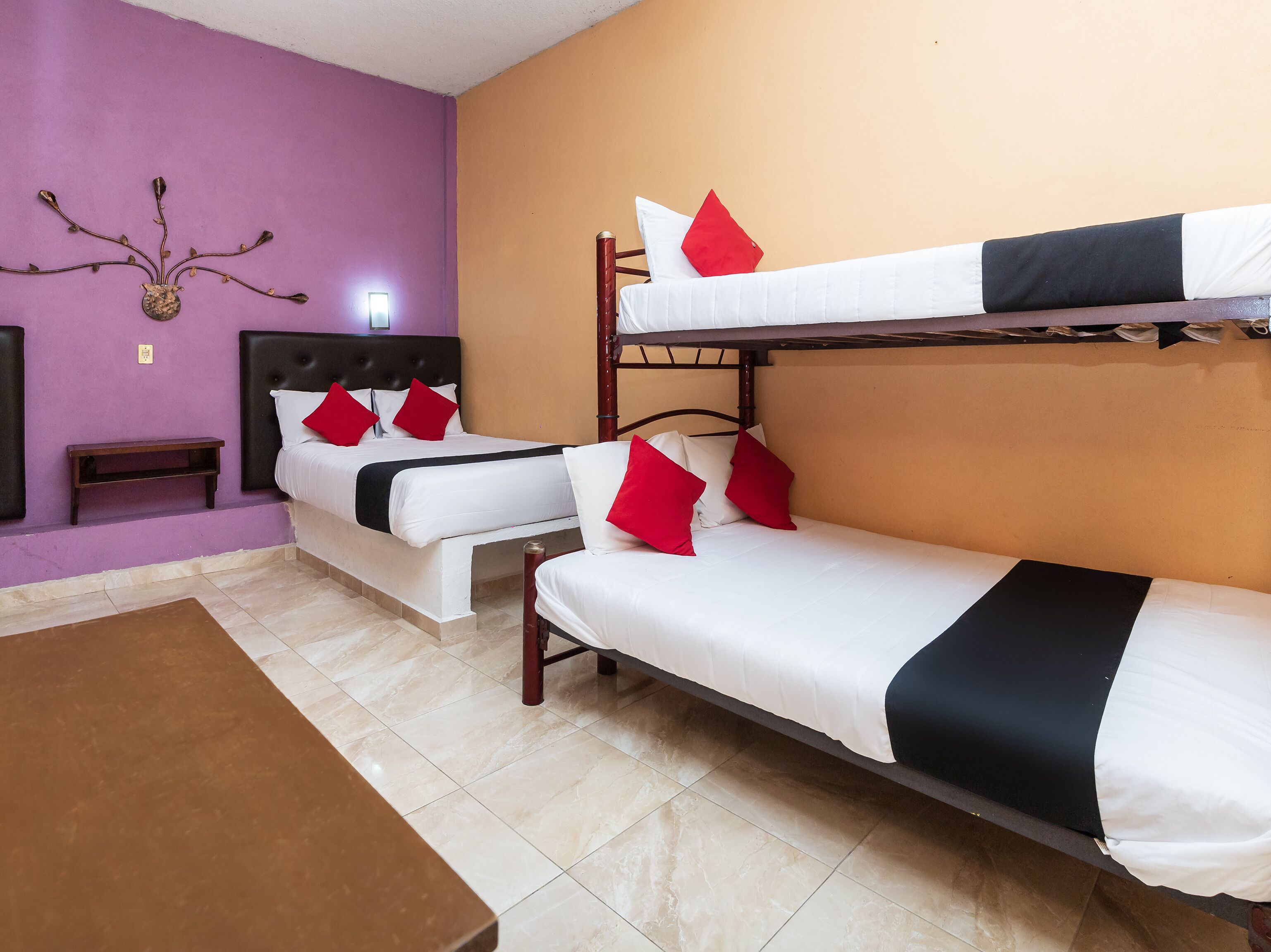 A hotel room with two single beds, a bunk bed, a wooden headboard, a small bedside table, and a brown table.