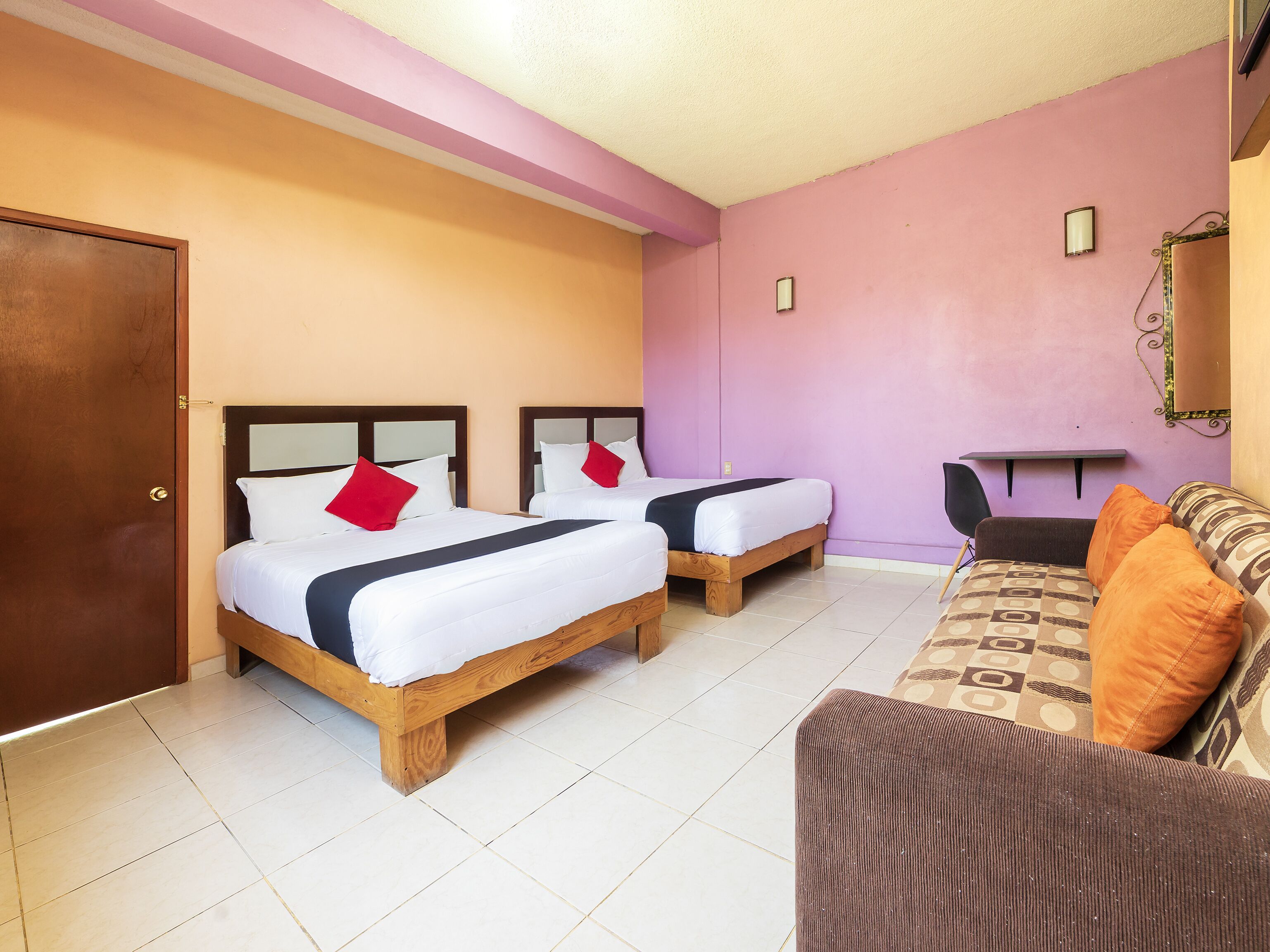 A hotel room with two wooden beds, a sofa, a desk, and a door.