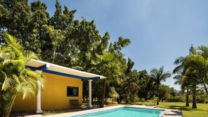 A swimming pool with a concrete deck, surrounded by lush greenery and a small building with a blue roof. - Villas el Paraíso, El Rollo (Tlaquiltenango)