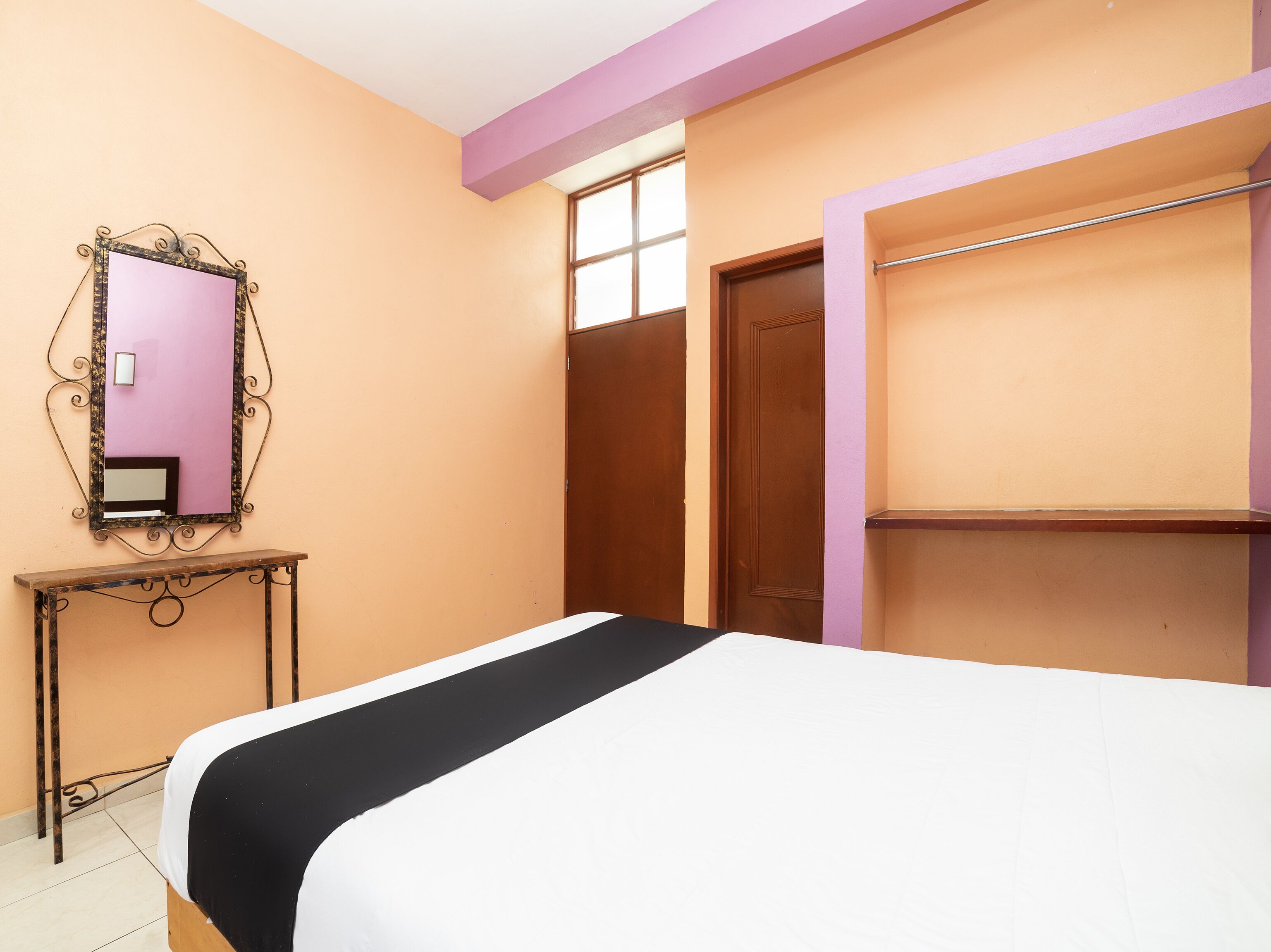 A bedroom with a bed, a wooden door, a mirror, and a shelf.