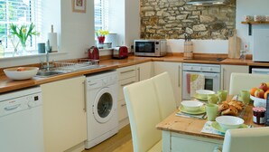Una cocina moderna con pared de piedra, lavadora, microondas y comedor con mesa lista para el desayuno.