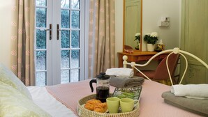 Un dormitorio con cama, una mesita de noche con un libro, una cafetera y una bandeja con croissants y tazas.
