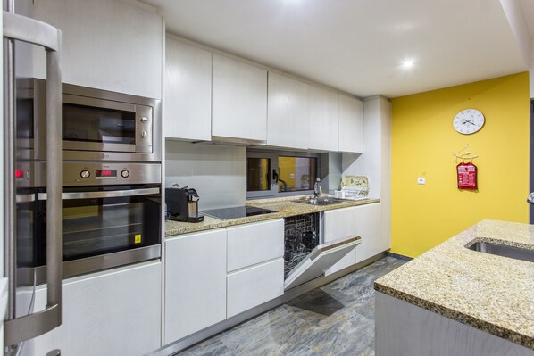 Una cocina moderna con electrodomésticos de acero inoxidable, lavavajillas y una pared de acento amarilla.