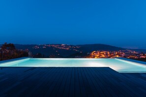 Una piscina con terraza de madera, con vistas a un paisaje urbano nocturno.