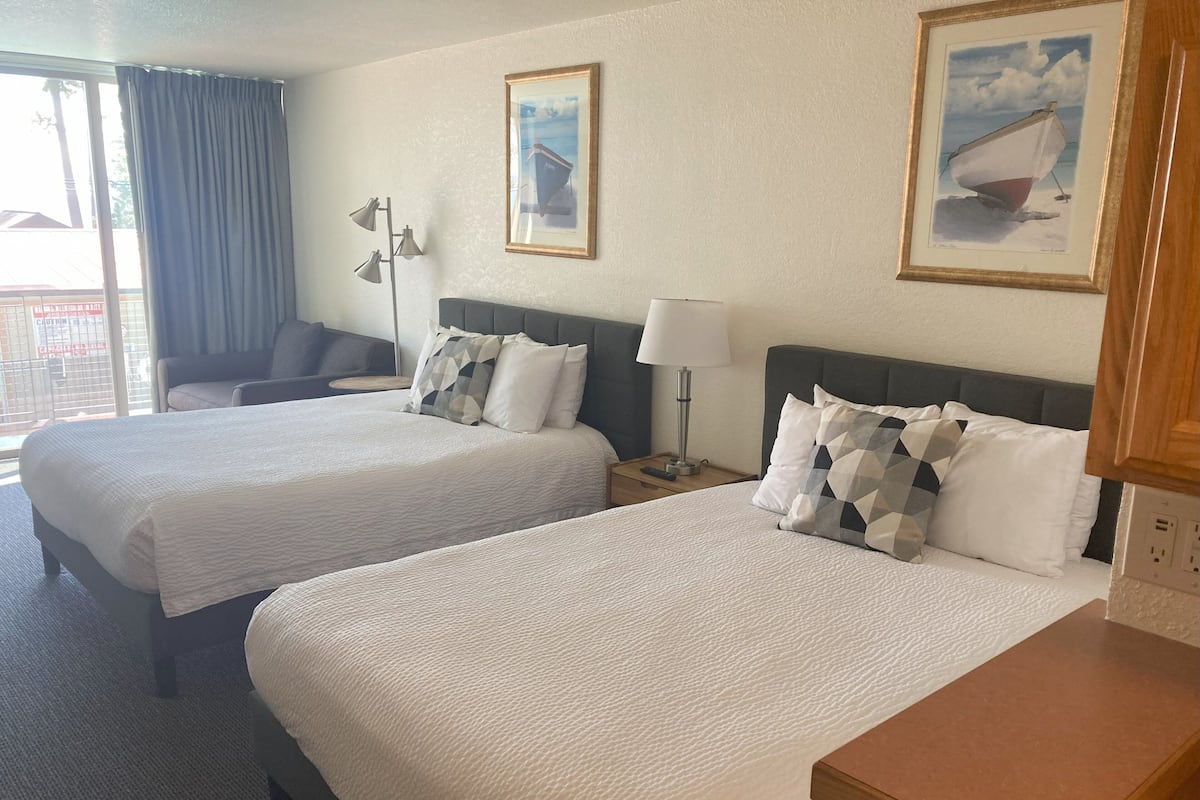 Une chambre d’hôtel avec deux lits, un bureau, une chaise et une fenêtre avec des rideaux.