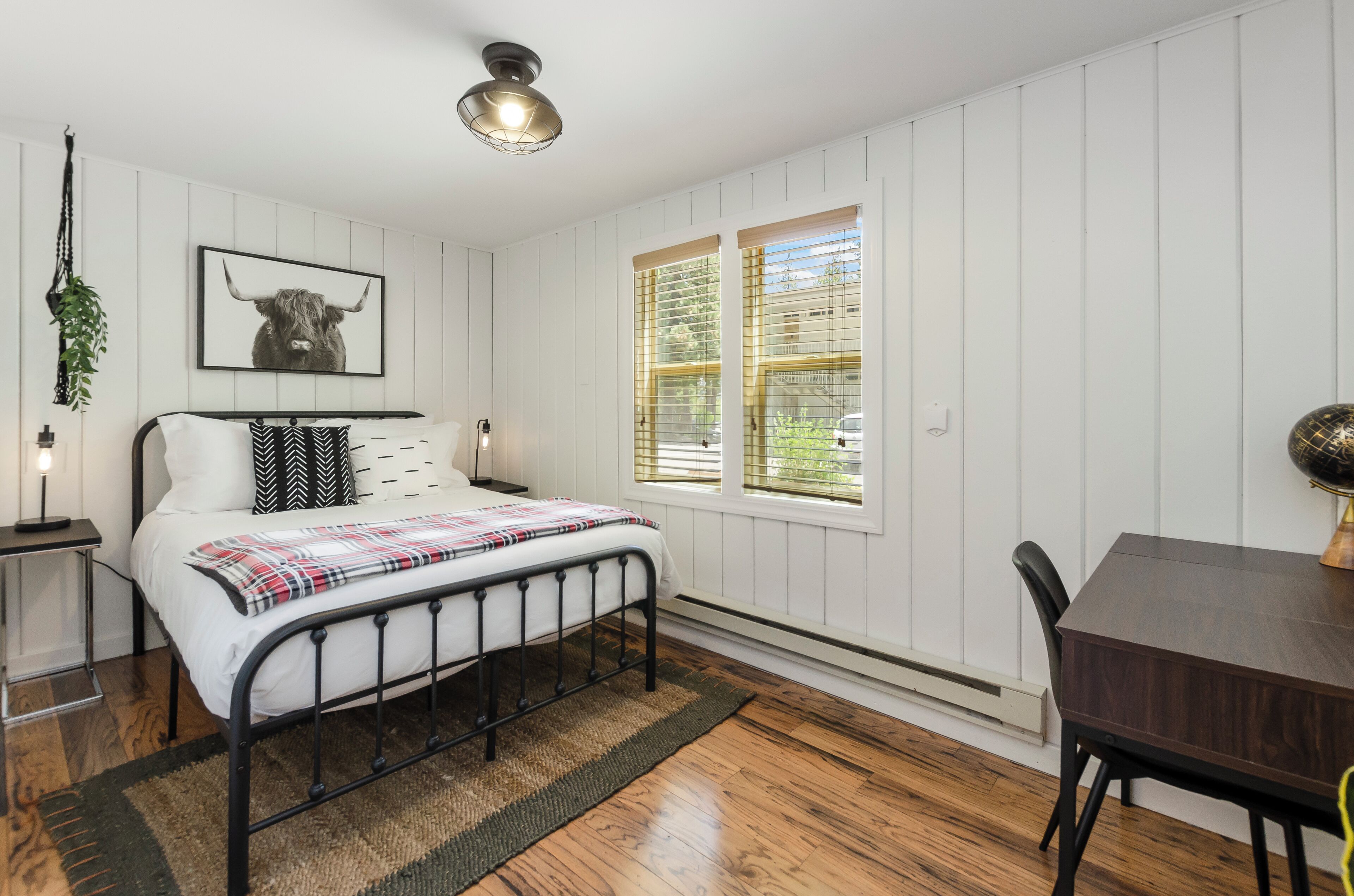 A bedroom with a bed, bedside table, lamp, and a window with blinds.