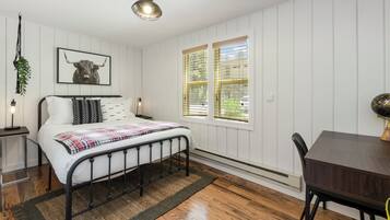 A bedroom with a bed, bedside table, lamp, and a window with blinds.
