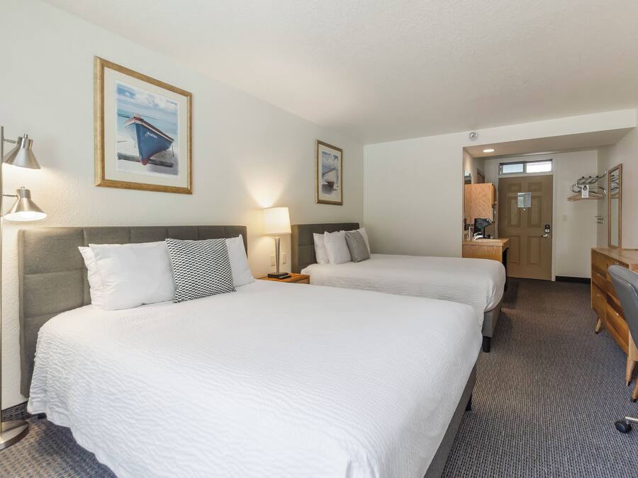 A hotel room with two beds, a desk, a chair, and a bathroom visible through an open door.