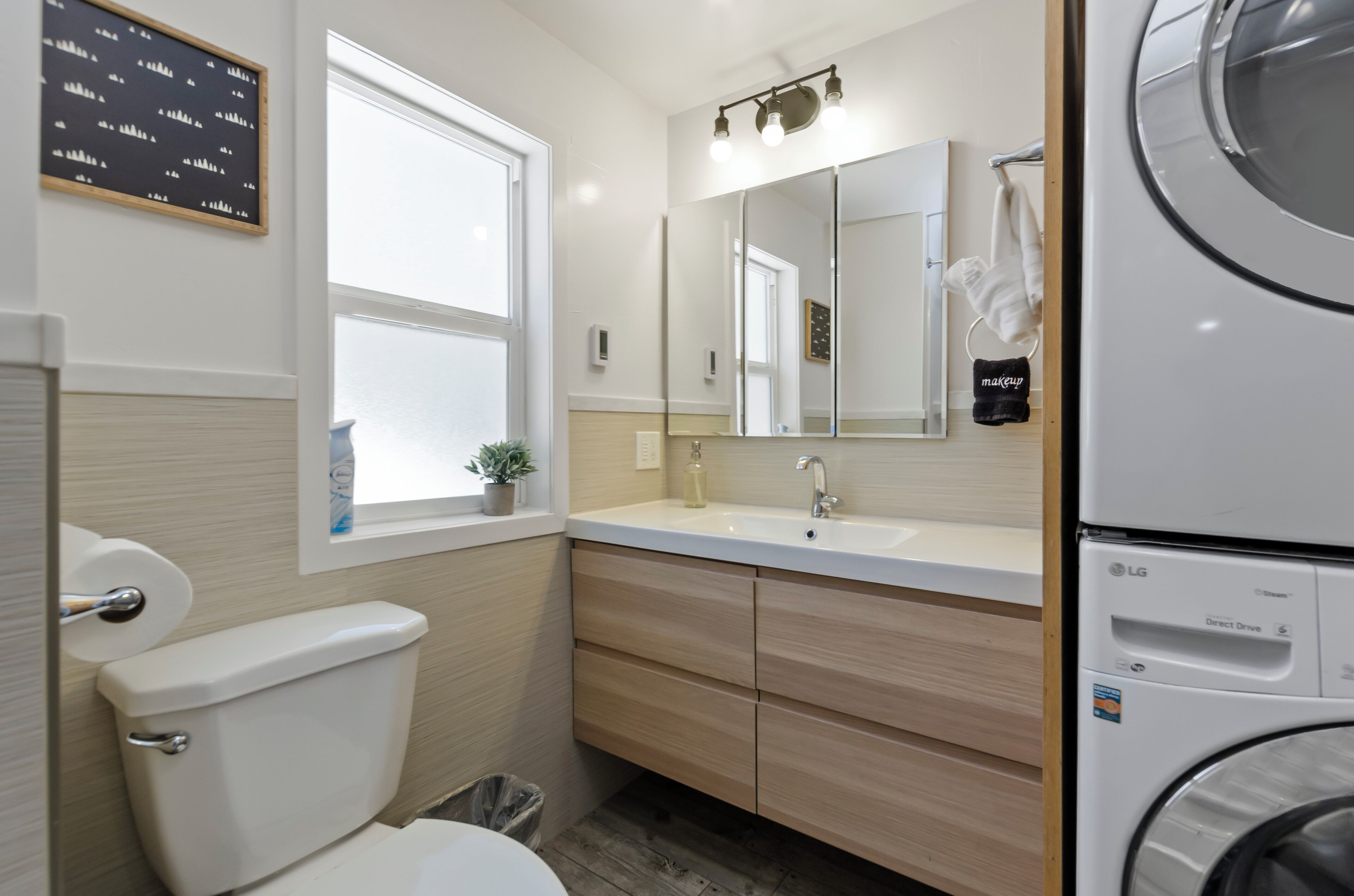 Ein modernes Badezimmer mit Toilette, Waschbecken, Spiegel und Waschmaschine.