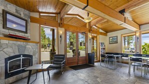 A spacious indoor area with a stone fireplace, wooden ceiling beams, and a view of the outdoors through large glass doors. - Firelite Lodge (Kings Beach)