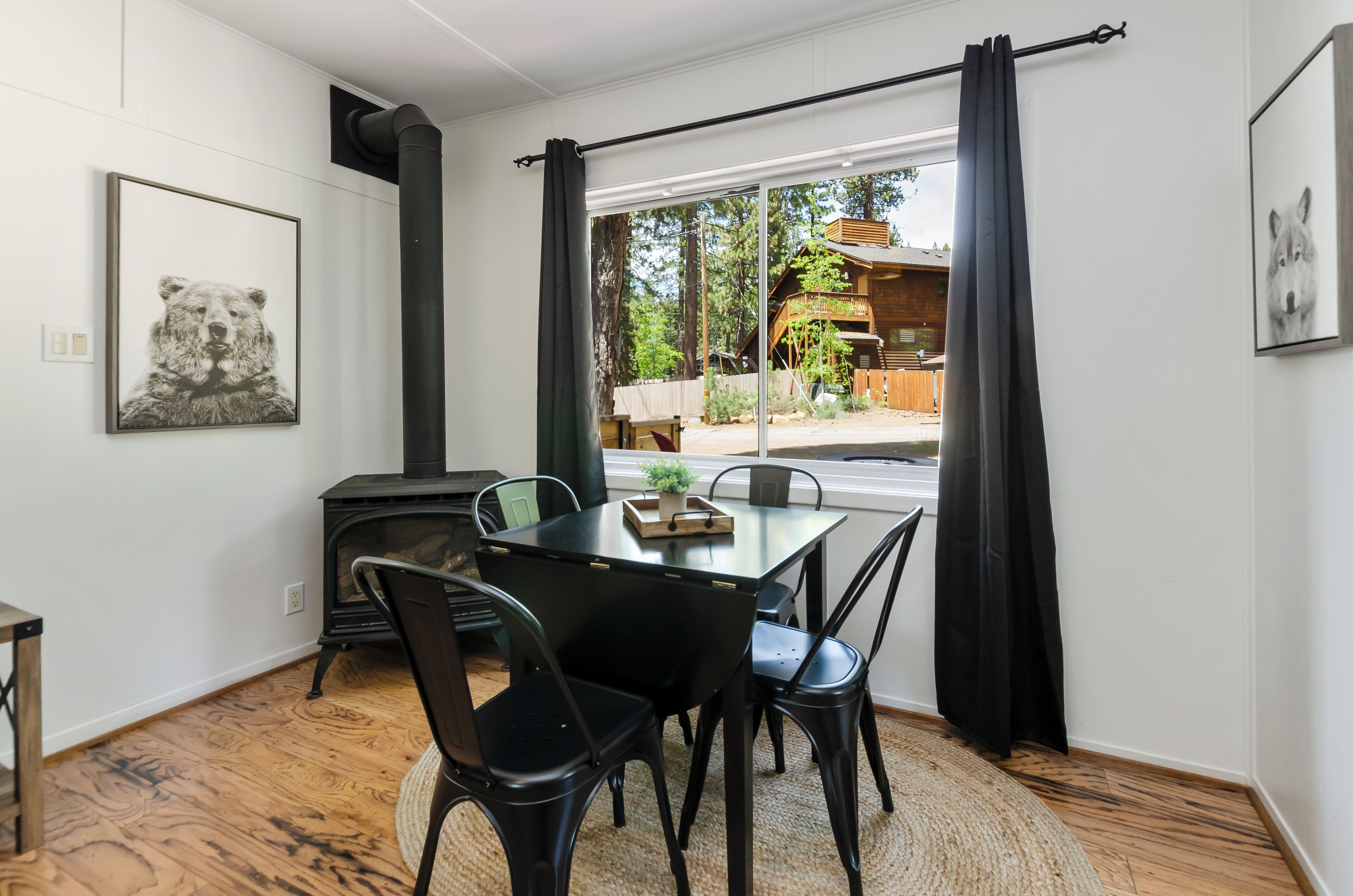 A dining area with a table and chairs, a fireplace, and a view of a wooden cabin through large windows.