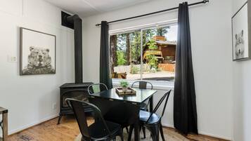 A dining area with a table and chairs, a fireplace, and a view of a wooden cabin through large windows.
