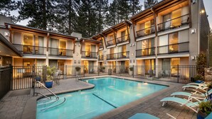 A multi-story hotel with a swimming pool, outdoor seating, and a view of tall trees. - Firelite Lodge (Kings Beach)