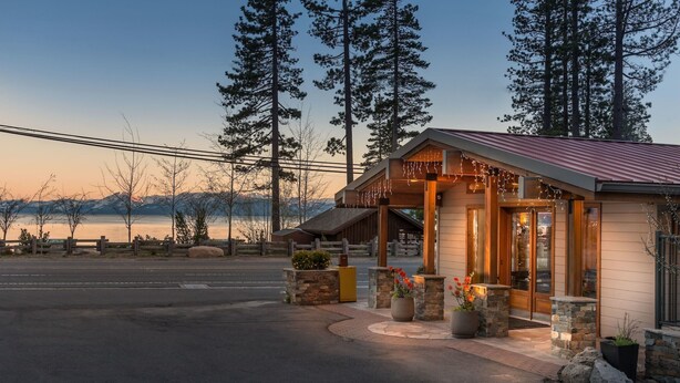 A lodge with a stone facade, wooden porch, and a view of a lake at dusk. - Firelite Lodge (Kings Beach)
