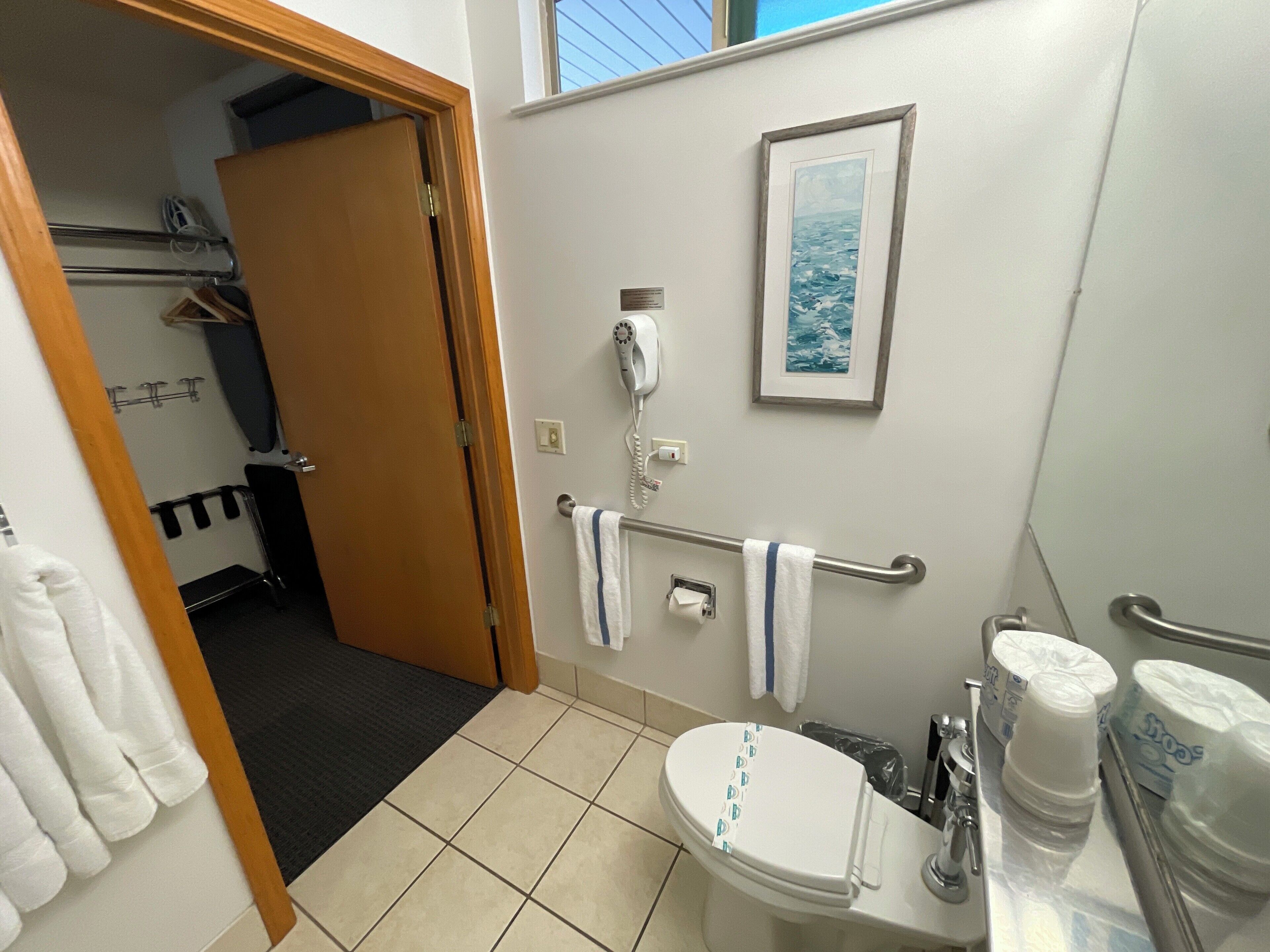 Un bagno con un water, un asciugatore di mani e un quadro appeso al muro.