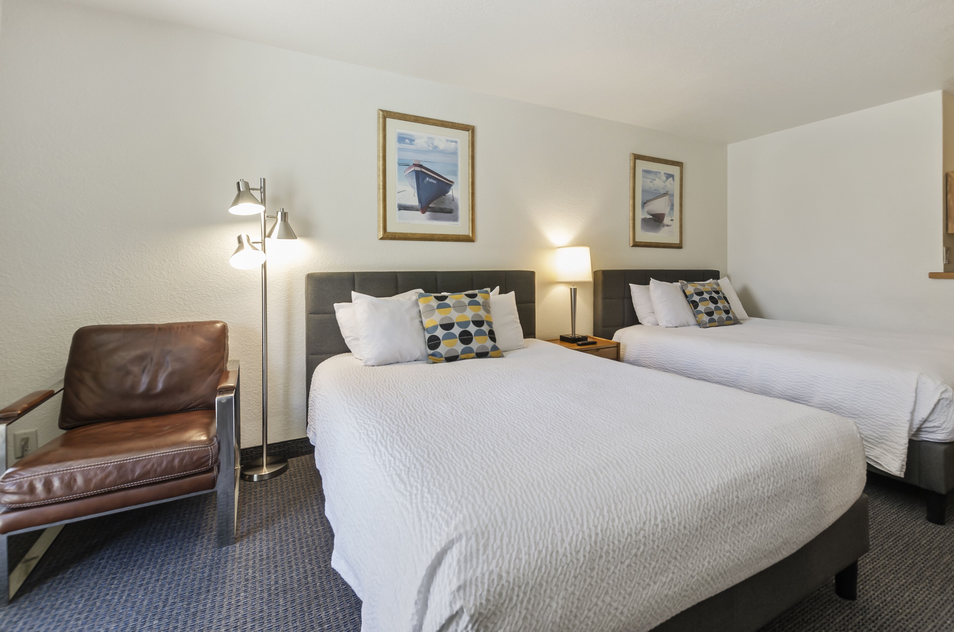 A hotel room with two beds, a brown leather chair, and a floor lamp.