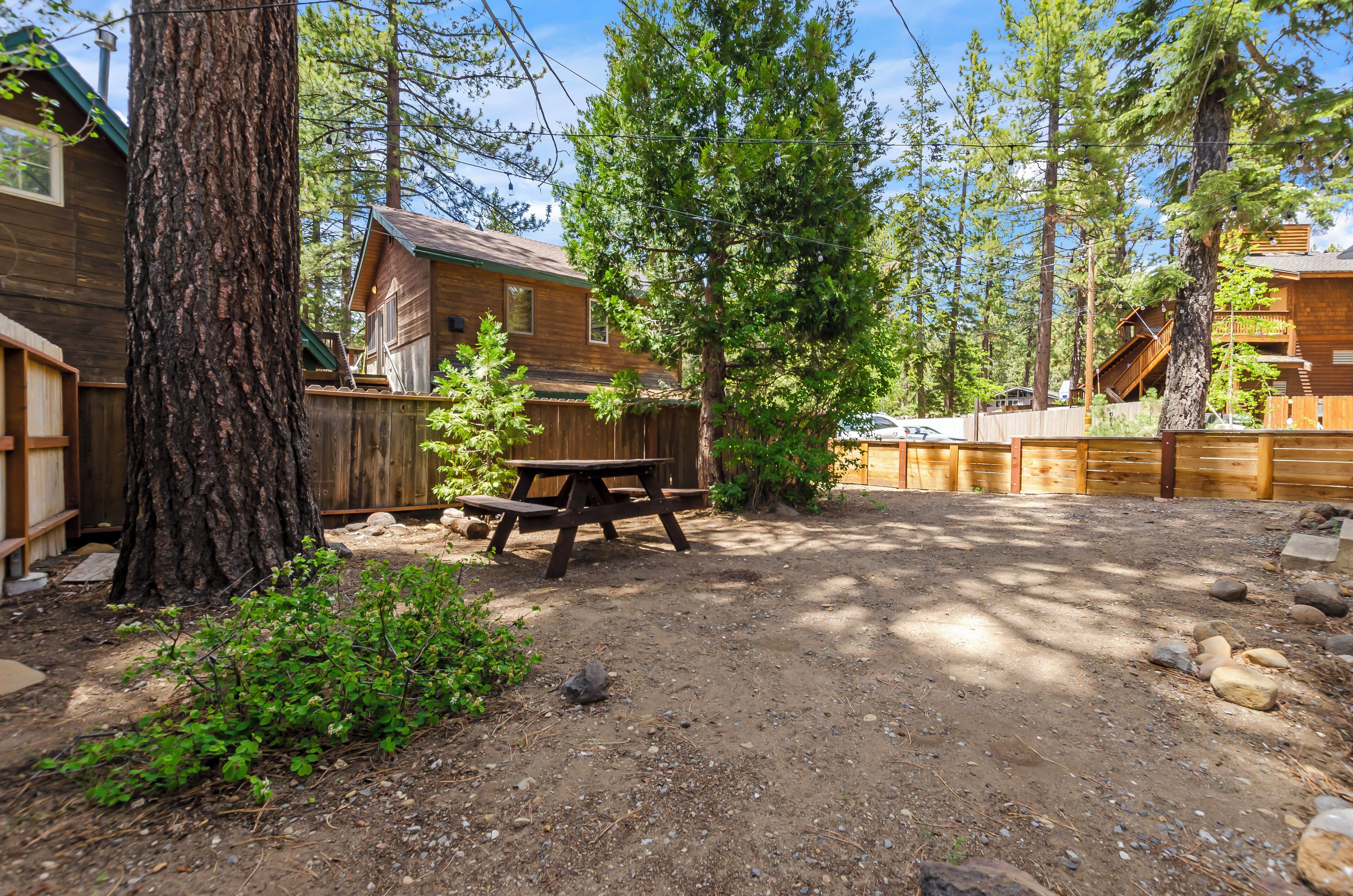 A rustic cabin with a wooden deck, surrounded by trees and a picnic table.