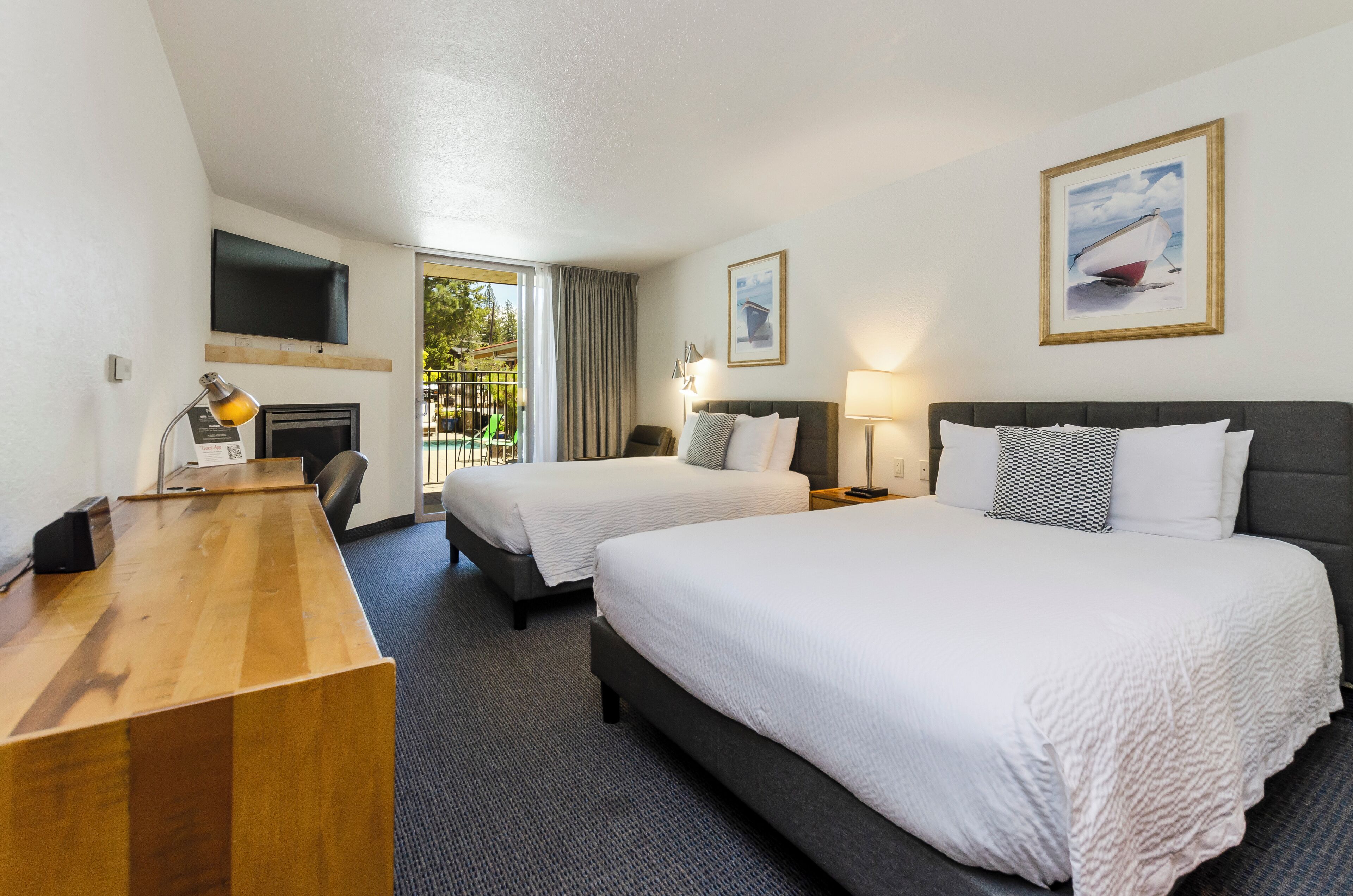 A hotel room with two beds, a desk, a flat-screen TV, and a painting of a sailboat.