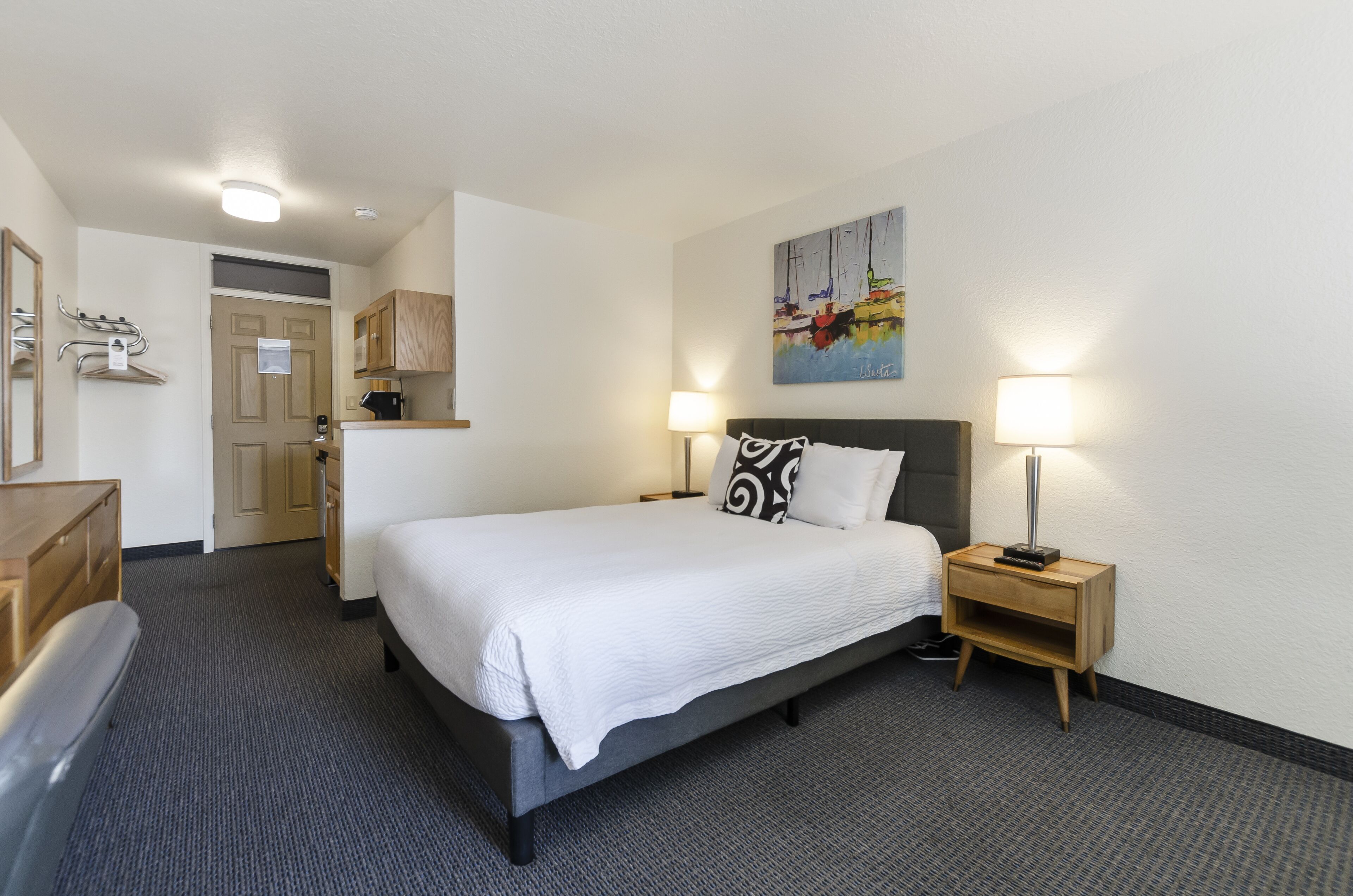 Quarto de hotel com cama, mesa de cabeceira, luminária e um quadro na parede.