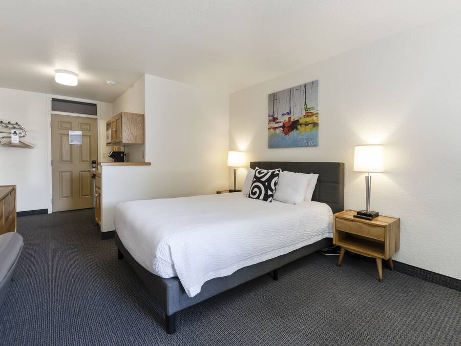 Hotellihuone, jossa on sänky, yöpöytä, lamppu ja taulu seinällä.