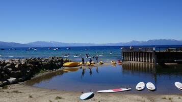 Una playa con kayaks y tablas de surf, una costa rocosa y un muelle que se adentra en el agua.