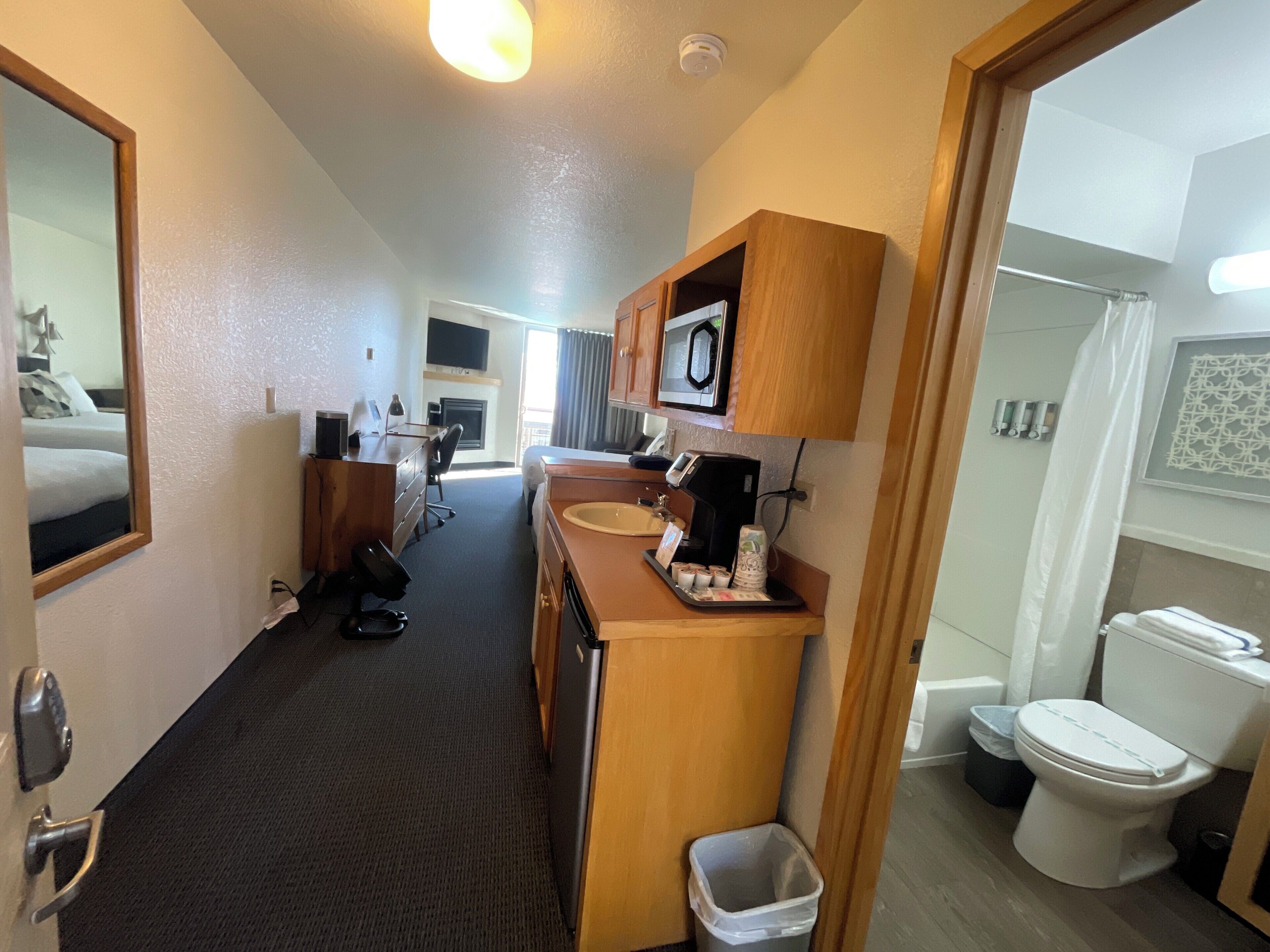 A hotel room with a bed, desk, chair, microwave, sink, and toilet.