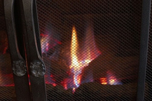 Primer plano de una parrilla metálica con fuego a sus espaldas.