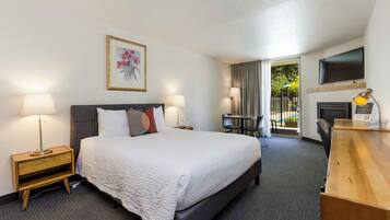 A hotel room with a large bed, bedside lamps, a desk with a chair, a flat-screen TV, and a window with curtains.