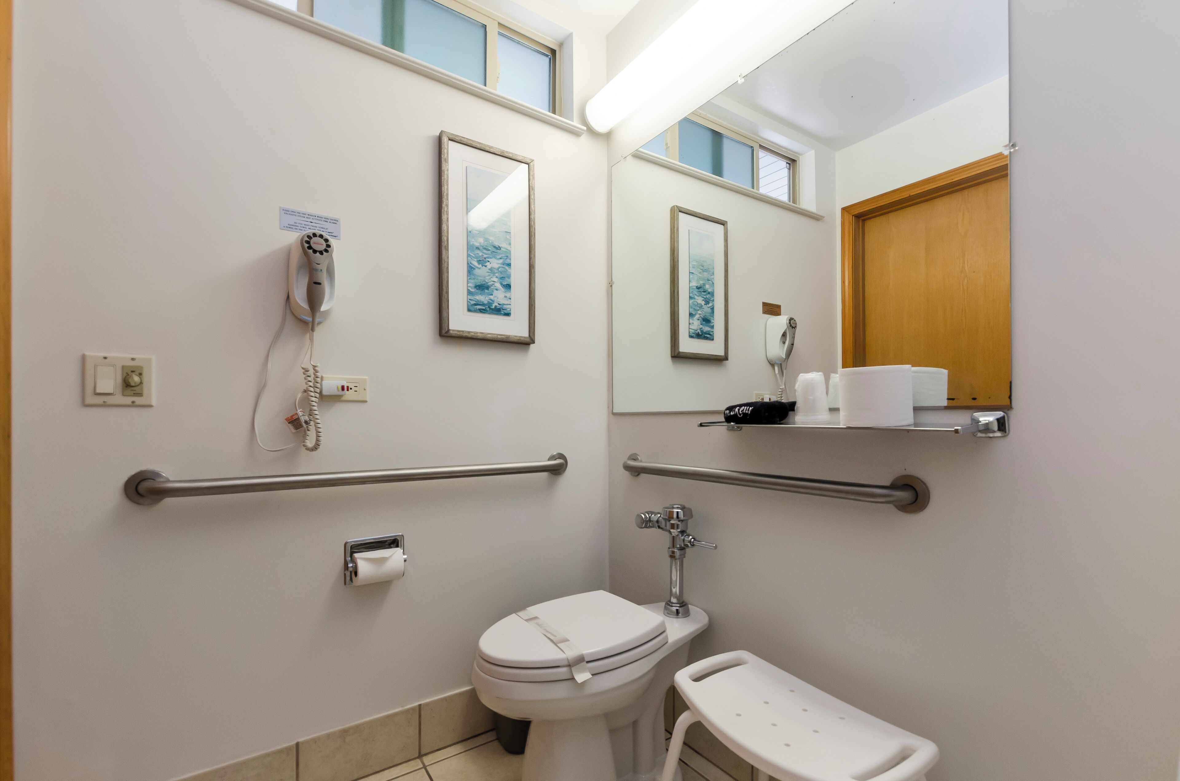 A bathroom with a toilet, hand dryer, and handrails.