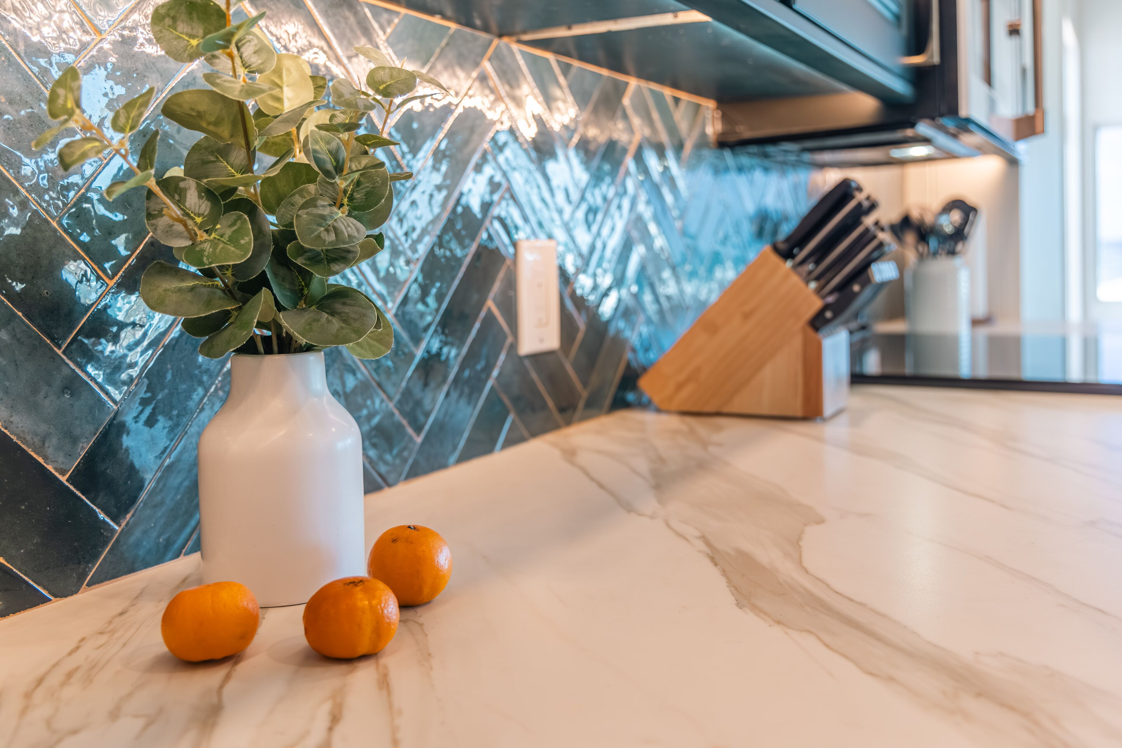 Una encimera de cocina con un jarrón blanco que contiene plantas verdes y tres naranjas.
