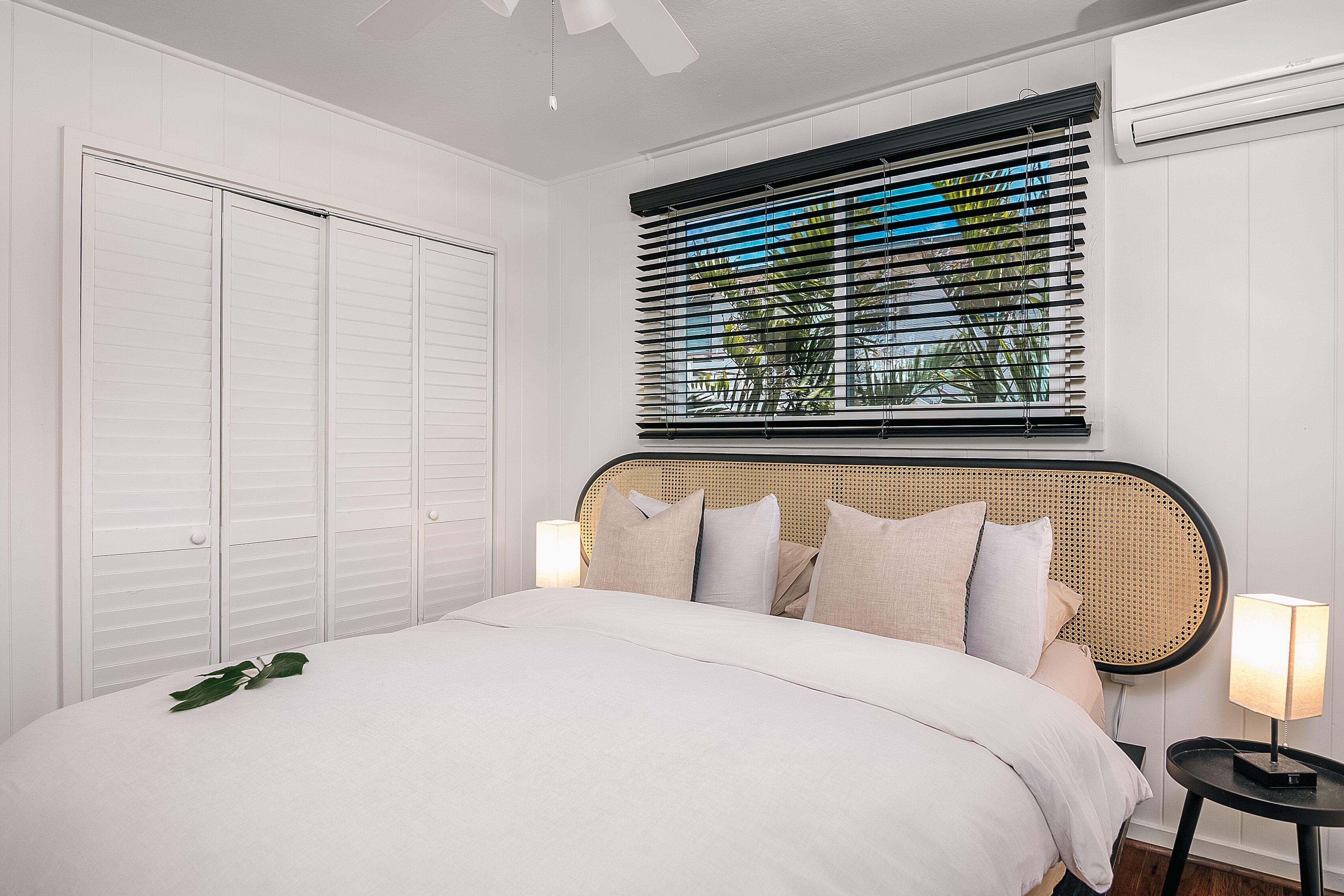 Een slaapkamer met een bed, nachtkastje met lamp, raam met zonwering en een kledingkast.