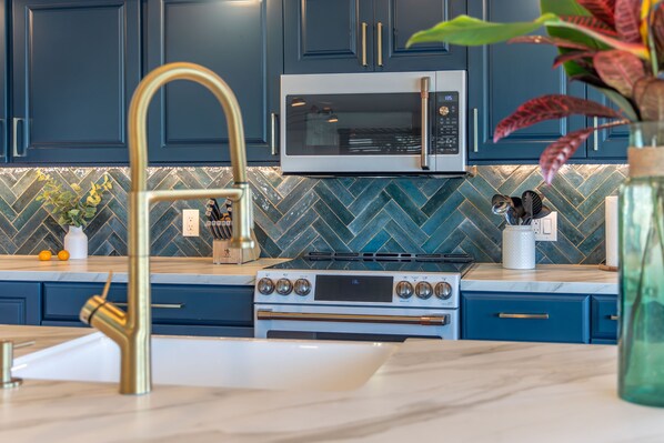 Une cuisine avec des meubles de couleur bleu foncé, un four à micro-ondes en acier inoxydable, une cuisinière à gaz et un plan de travail en marbre.