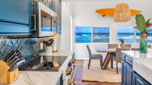 Una cocina moderna con vista al océano, que incluye un adorno con forma de tabla de surf, una zona de comedor con vistas y una variedad de electrodomésticos.