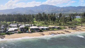 Una propiedad costera con casas frente a la playa, una playa de arena y montañas al fondo.