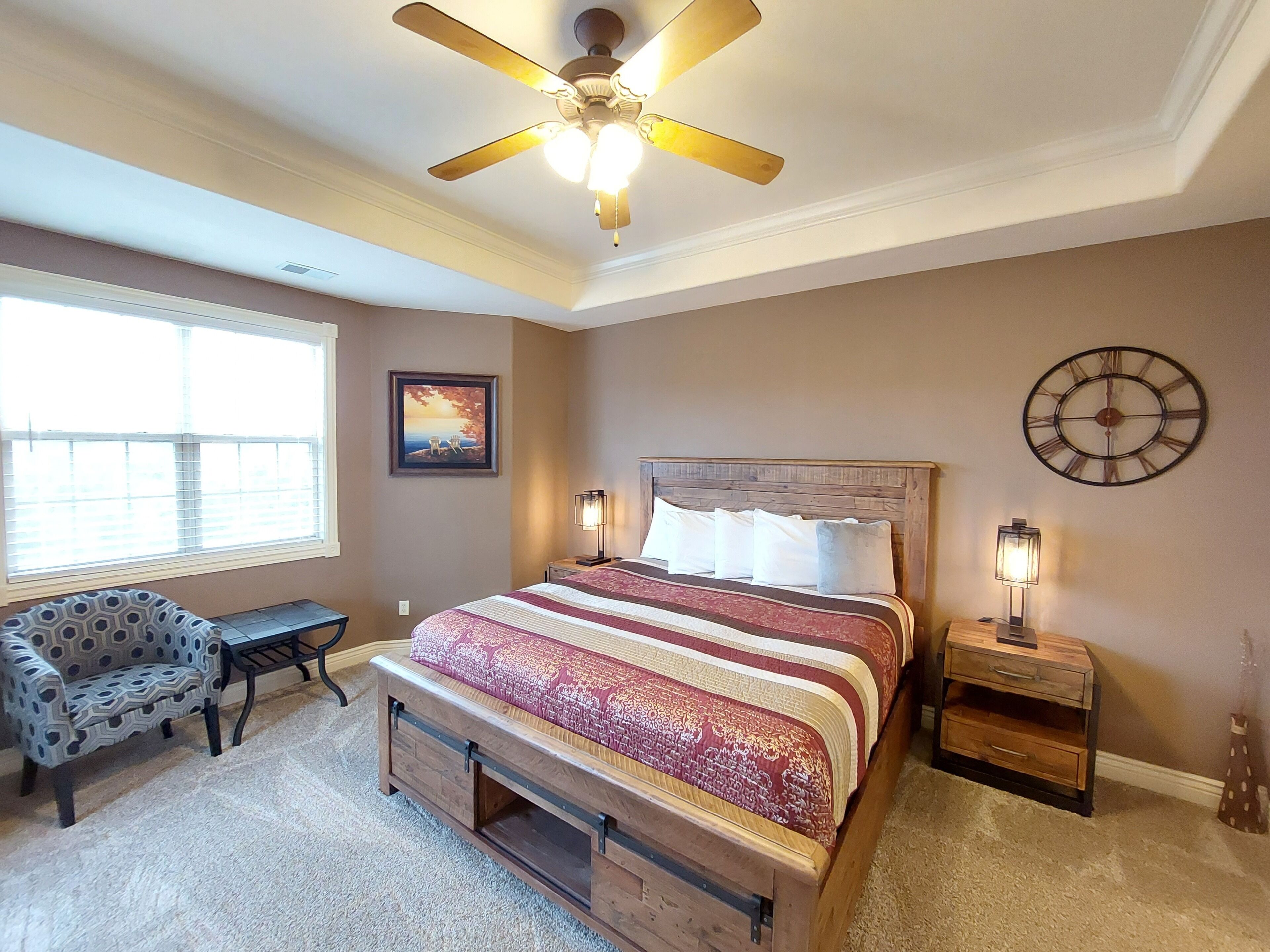 A bedroom with a bed, a chair, a desk, a clock, and a ceiling fan.
