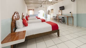 A hotel room with four beds, a desk, a TV, and a ceiling fan.