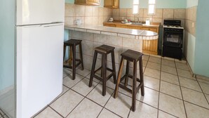A kitchen with a refrigerator, wooden cabinets, a stove, and two stools. - Hotel Posada Agua Escondida (Cihuatlan)
