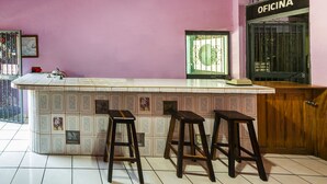 A kitchen with a pink wall, a tiled backsplash, and three wooden stools. - Hotel Posada Agua Escondida (Cihuatlan)