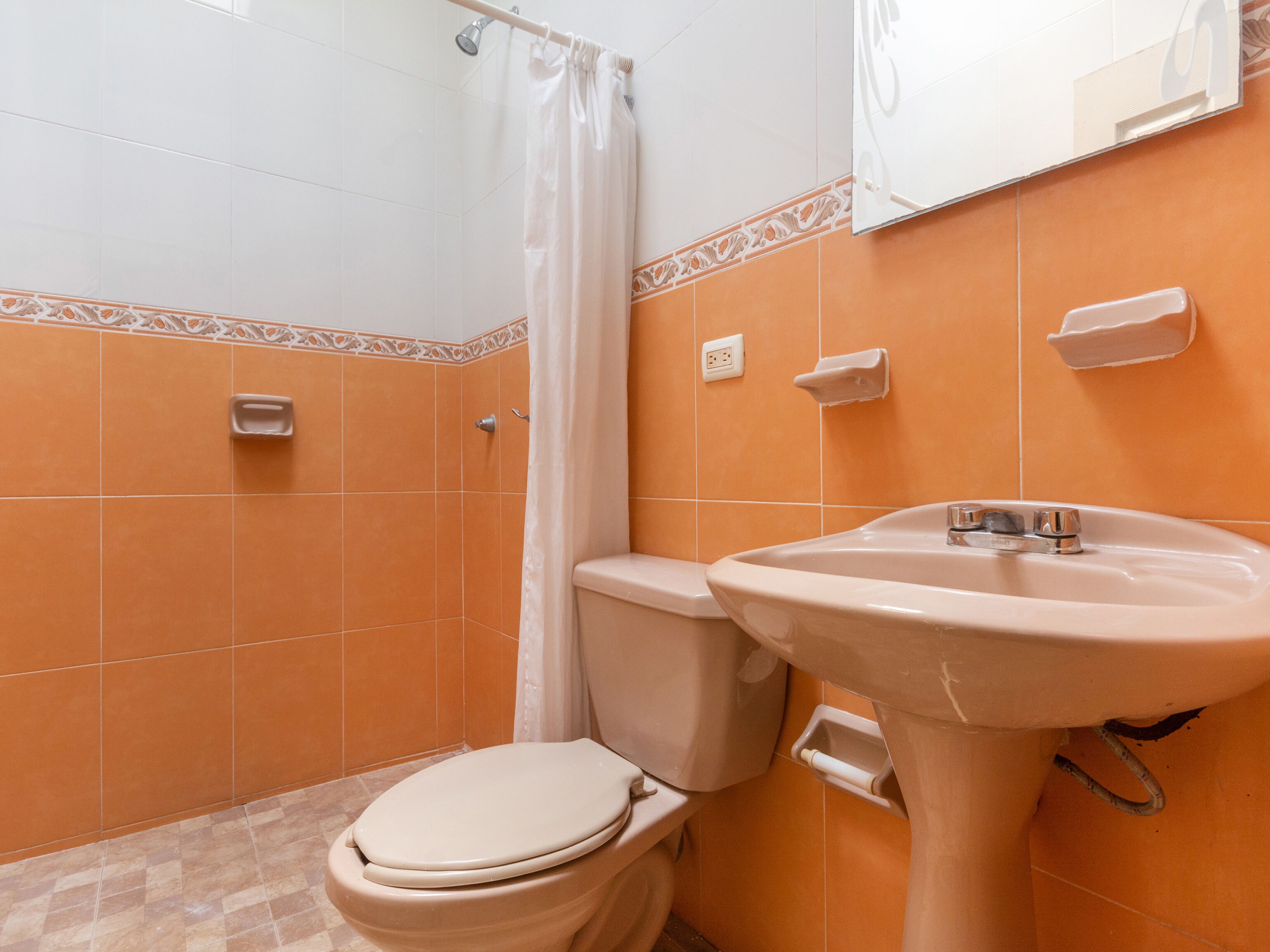 Et badeværelse med orange fliser, toilet, vask og bruseforhæng.