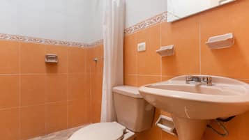Et badeværelse med orange fliser, toilet, vask og bruseforhæng.