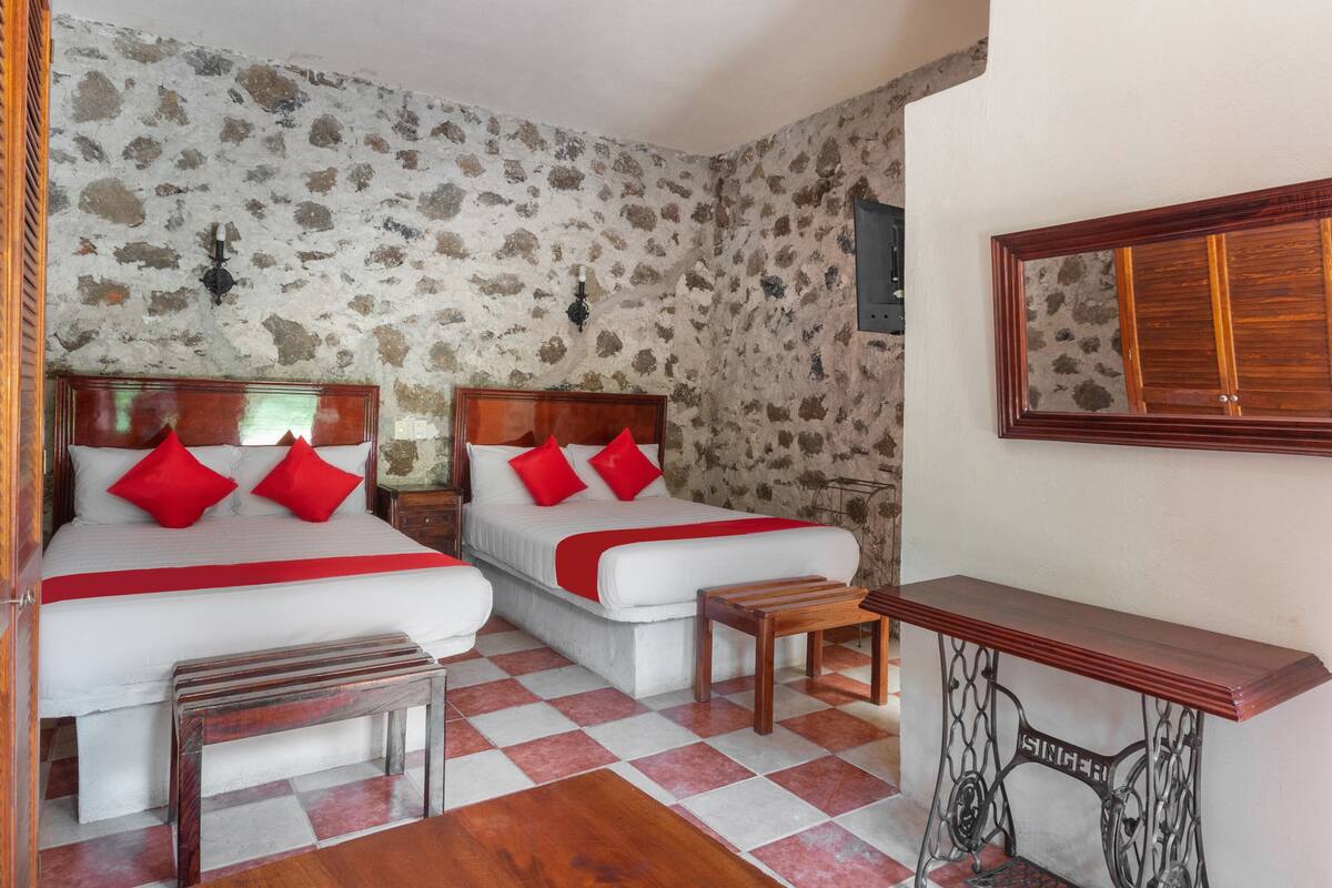 A room with two beds, a wooden bench, a sewing machine, and a mirror on the wall.