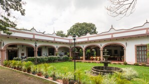 A courtyard with a fountain, potted plants, and a building with arches and columns. - Rancho Hotel El Carmen (Tlapacoyan)