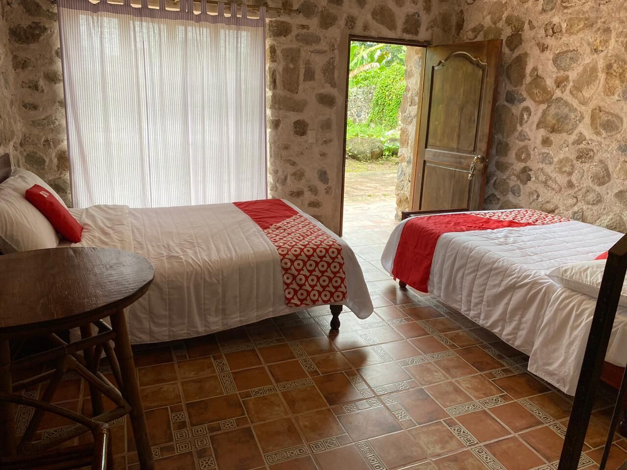 A room with two beds, a wooden table, and a stone wall.
