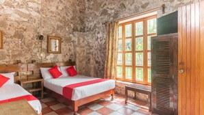 A rustic room with a large window, a wooden bed with red pillows, a small table, and a wooden wardrobe. - Rancho Hotel El Carmen (Tlapacoyan)