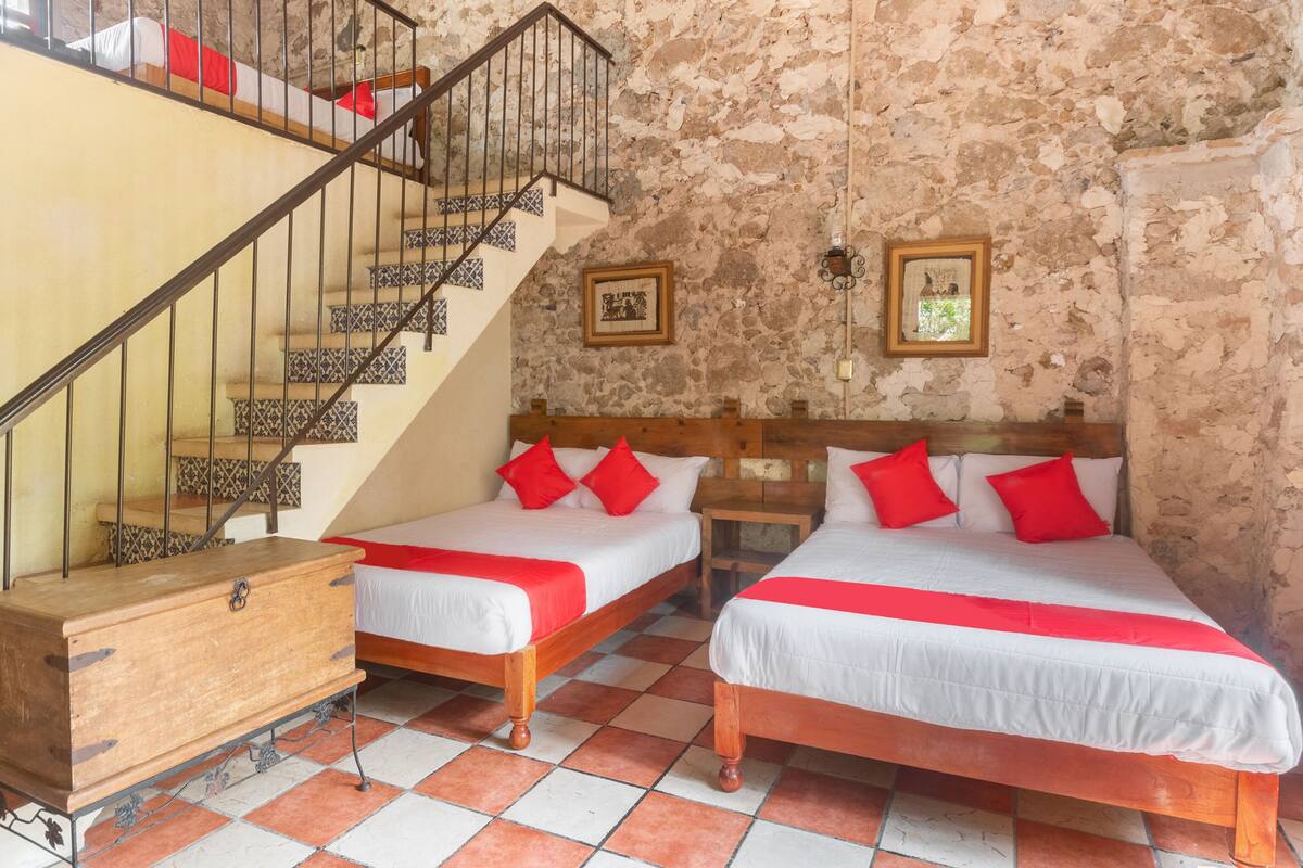 A room with two beds, a wooden dresser, a staircase with patterned tiles, and stone walls.