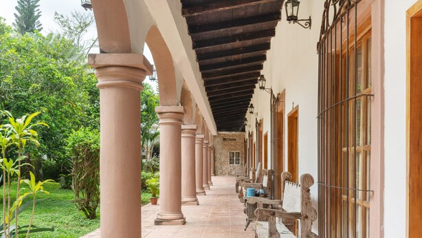 A covered corridor with columns, wooden benches, and potted plants. - Rancho Hotel El Carmen (Tlapacoyan)