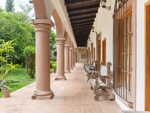 Un corredor cubierto con columnas, bancos de madera y plantas en macetas.